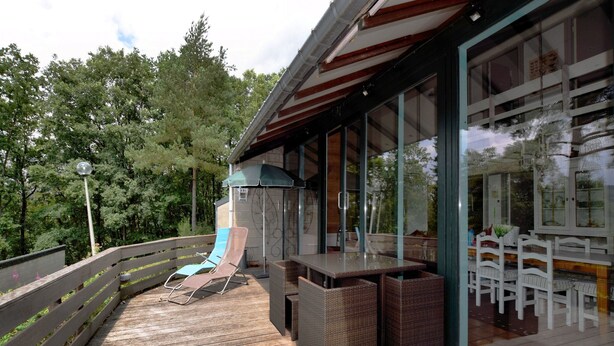 A wooden deck with outdoor furniture, a glass-enclosed dining area, and a view of trees.