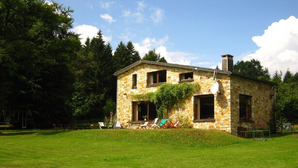 A stone house with a chimney, surrounded by a grassy lawn and trees. - Rustic Retreat in Houvegné (Stavelot)