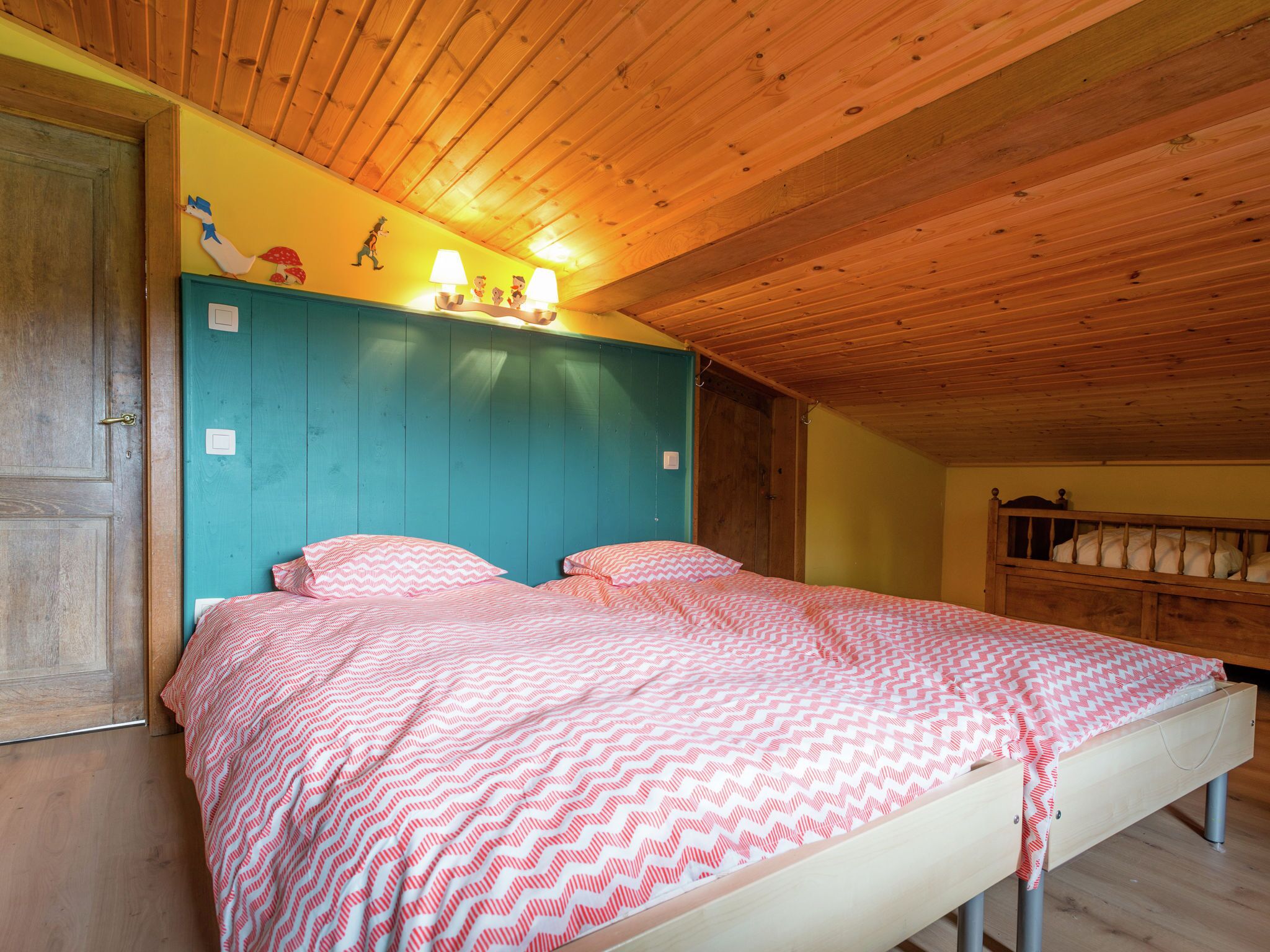 A bedroom with a wooden ceiling, a teal headboard, and a bed with pink patterned bedding.