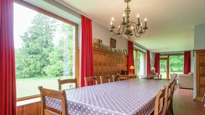 A dining room with a large table, wooden chairs, a chandelier, and large windows with red curtains. - Rustic Retreat in Houvegné (Stavelot)