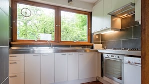 A kitchen with white cabinets, a double sink, a stove, and a window with a view of trees. - Rustic Retreat in Houvegné (Stavelot)
