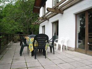 Eine Terrass mit Tisch und Stühlen, einer Holzhütte und einem weißen Gebäude mit großen Fenstern.