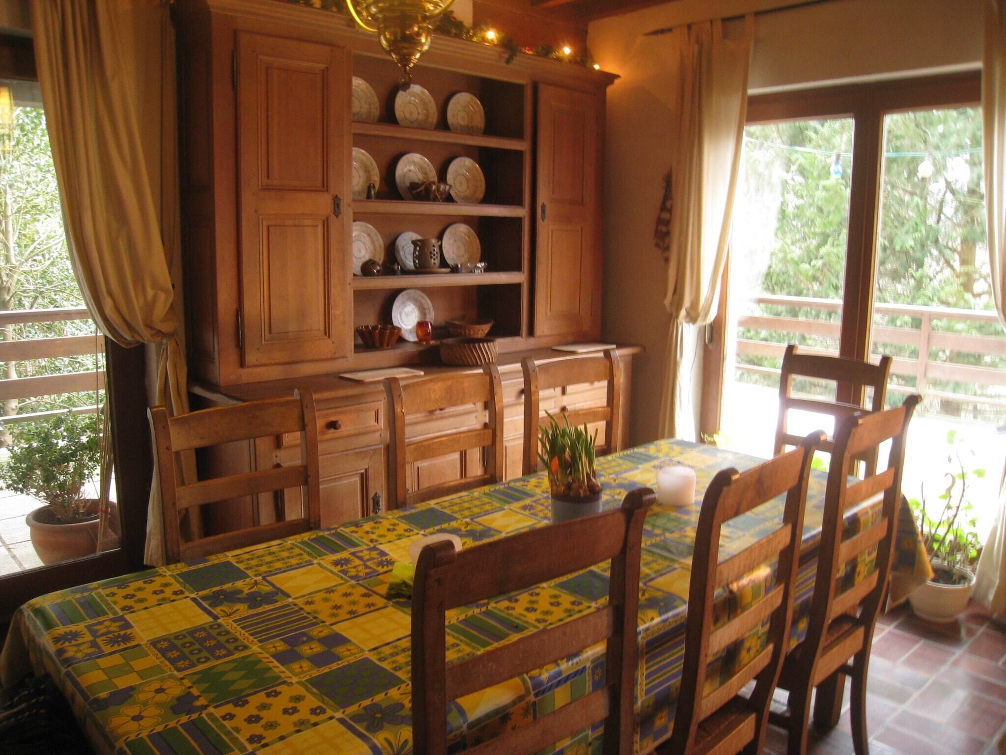 A dining area with a table set for four, wooden chairs, a patterned tablecloth, and a cabinet with dishes.