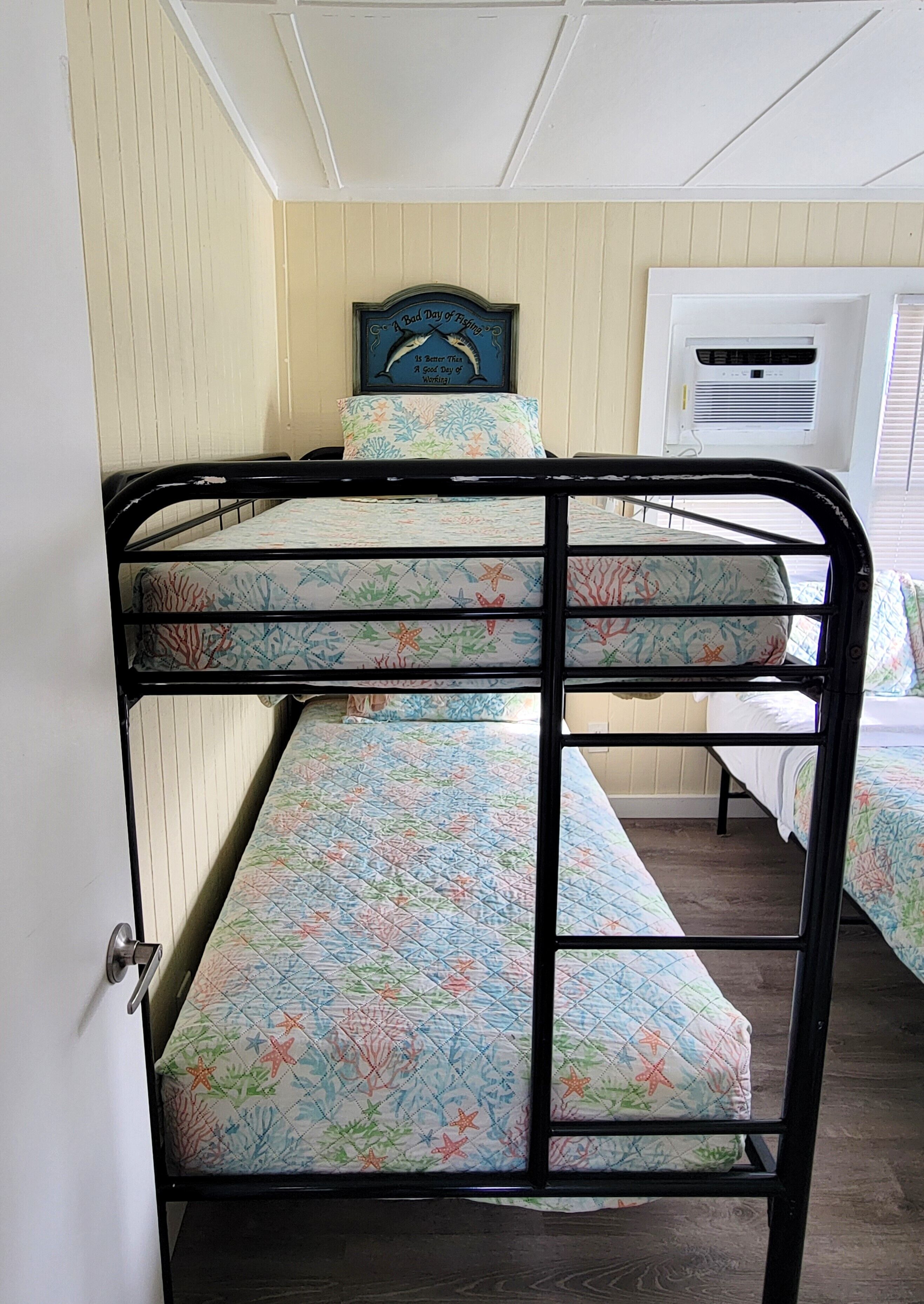 Un letto a castello con materasso a motivi floreali, una testiera decorativa con una citazione e un condizionatore d'aria sullo sfondo.