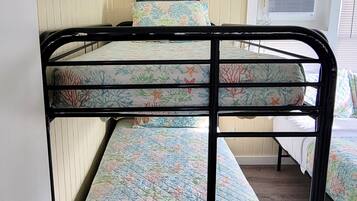 Un letto a castello con materasso a motivi floreali, una testiera decorativa con una citazione e un condizionatore d'aria sullo sfondo.