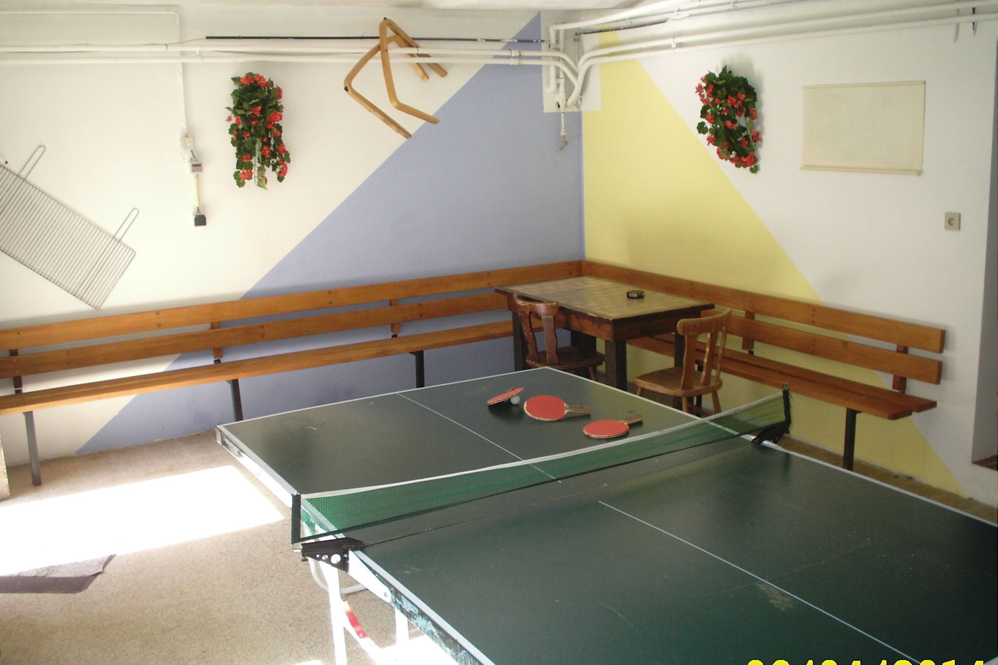 A ping pong table with two red paddles, a wooden bench, and a small table.