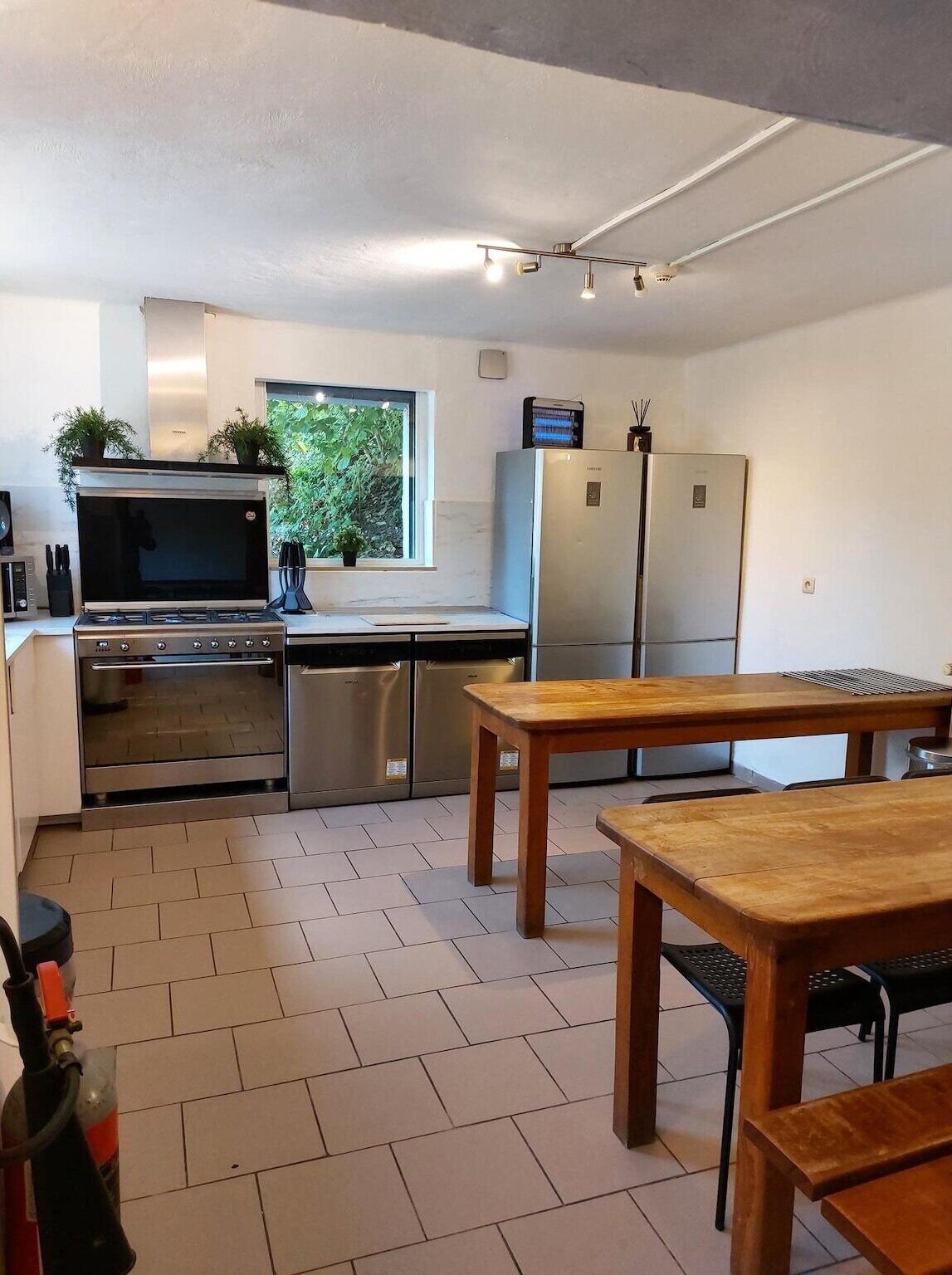 A modern kitchen with stainless steel appliances, a wooden table, and a window with a view of greenery.