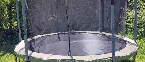 Un trampolín con red de seguridad, rodeado de césped y árboles.