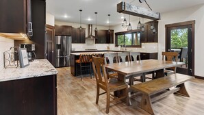 A modern kitchen with dark wood cabinets, stainless steel appliances, and a large island with bar stools. - Stylish home with hot tub, pool access, wifi and garage (Lead)