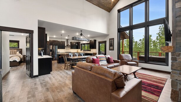 A spacious living area with a large window, a fireplace, and a dining area with a kitchen in the background. - Stylish home with hot tub, pool access, wifi and garage (Lead)