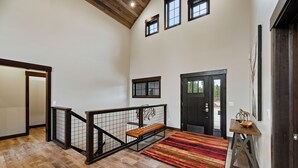 A spacious hallway with a wooden floor, a bench, a red striped rug, and a door with a dark frame. - Stylish home with hot tub, pool access, wifi and garage (Lead)