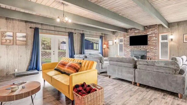 Una sala de estar acogedora con un sofá amarillo, sofás grises, techo de madera y chimenea.