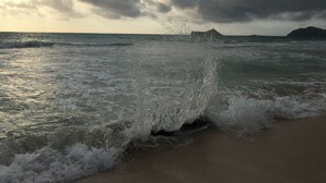 Una playa con olas rompiendo en la orilla y una montaña distante bajo un cielo nublado.