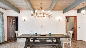 Comedor con mesa de madera, sillas blancas, una araña y apliques de pared.