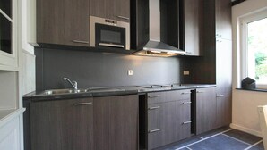 A modern kitchen with dark wood cabinets, a stainless steel sink, and a built-in microwave. - Namur Mansion by the Meus (Hastière par Dela)