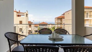 Ein Balkon mit Glastisch und Korbstühlen, der auf einen Wohnbereich mit Gebäuden und blauem Himmel blickt.