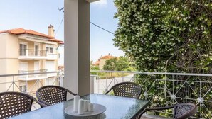 Ein Balkon mit Glastisch, Korbstühlen und einem weißen Geländer.