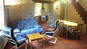 A rustic interior with a stone wall, wooden beams, a sofa, chairs, a small table, and a kitchen area. - Alpine Getaway in Neustift (Treignes)