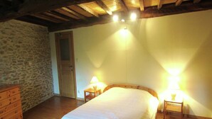 A bedroom with a wooden bed, two bedside lamps, a wooden dresser, and a stone wall. - Alpine Getaway in Neustift (Treignes)