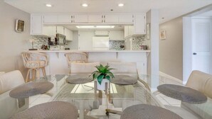 A modern kitchen with white cabinets, a glass dining table, and wicker chairs. - Silver Sands Sanctuary: Ocean + Pool Balcony Views (New Smyrna Beach)