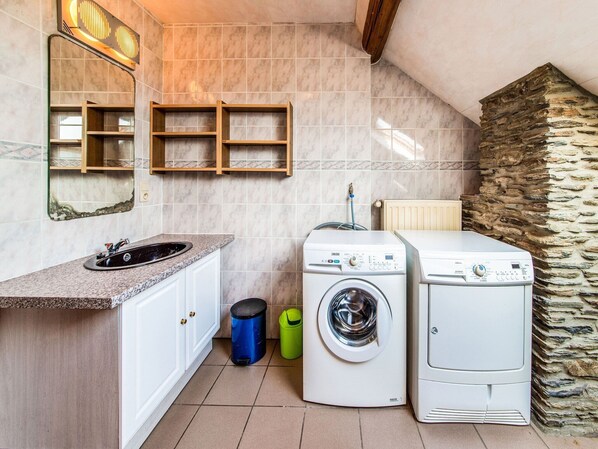 A compact laundry room with a sink, two washing machines, and a stone wall.