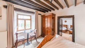 A bedroom with a wooden bed, a round table with chairs, a window with curtains, and a wardrobe.