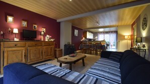 A living room with a sofa, a television, wooden cabinets, a dining area, and a kitchen. - Beautiful gîte in former farmhouse with garden (Sainte ode)