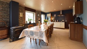 Un coin repas avec une table dressée pour quatre personnes, un poêle à bois et une cuisine en arrière-plan.