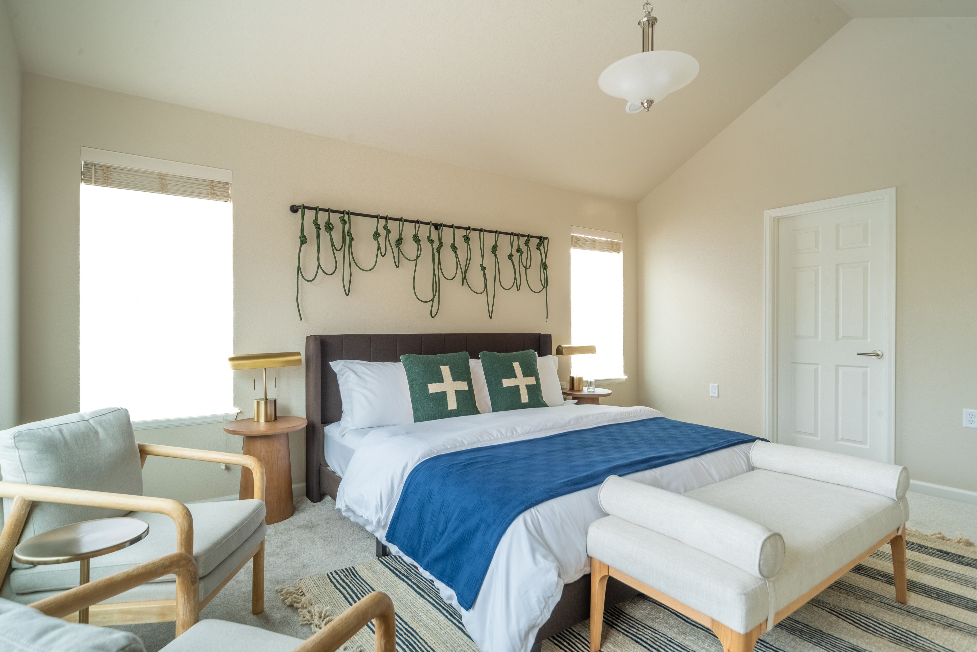 A bedroom with a bed, two bedside tables, a chair, a lamp, and a door.