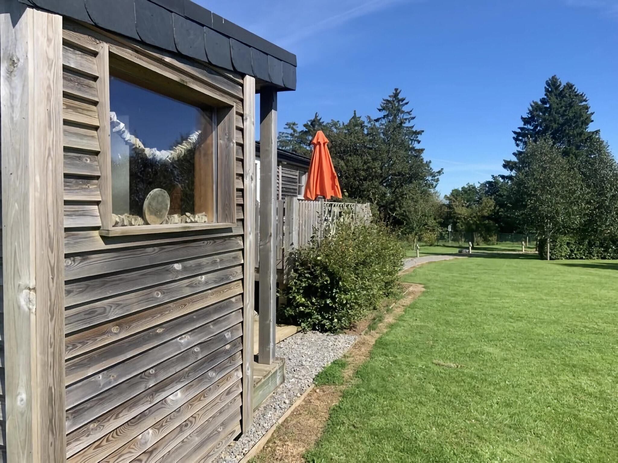 A wooden cabin with a window and a door, surrounded by a well-maintained lawn and trees.