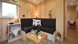 A cozy room with a dark brown sofa, a wooden table with glasses and bottles, a window with a view, and a wooden wall with a decorative panel. - Tranquil Stay in Vielsalm (Vielsalm)