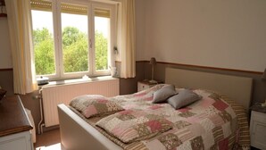 Een slaapkamer met een bed, een nachtkastje, een raam met gordijnen en een radiator.