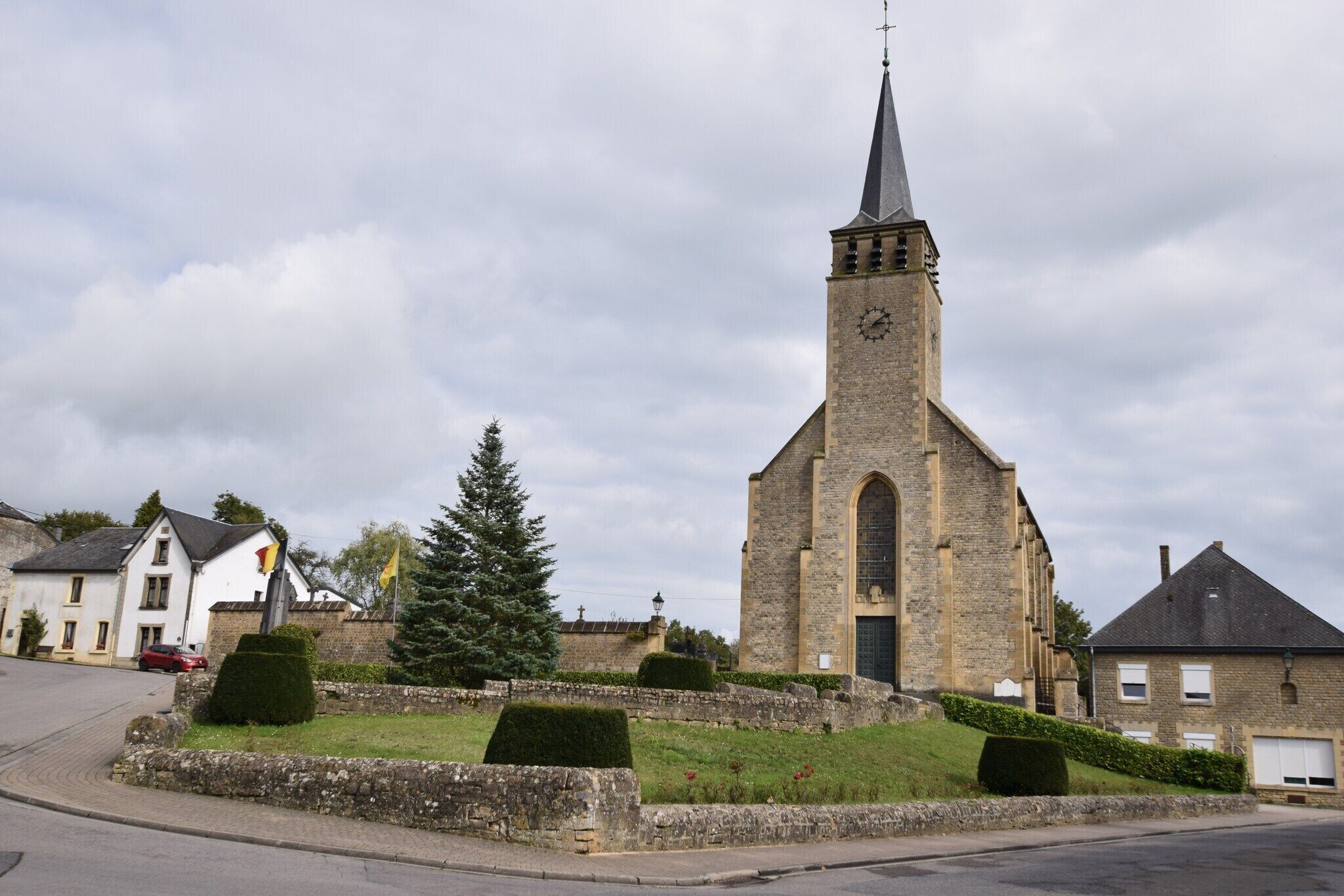 A church with a tall steeple and a clock, surrounded by a stone wall and greenery.