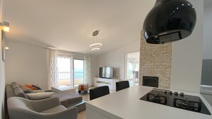 A modern kitchen with a central island, a dining area with chairs, a sofa, and a TV.