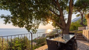 An outdoor dining area with a table and chairs, overlooking a scenic view of the sea and mountains.