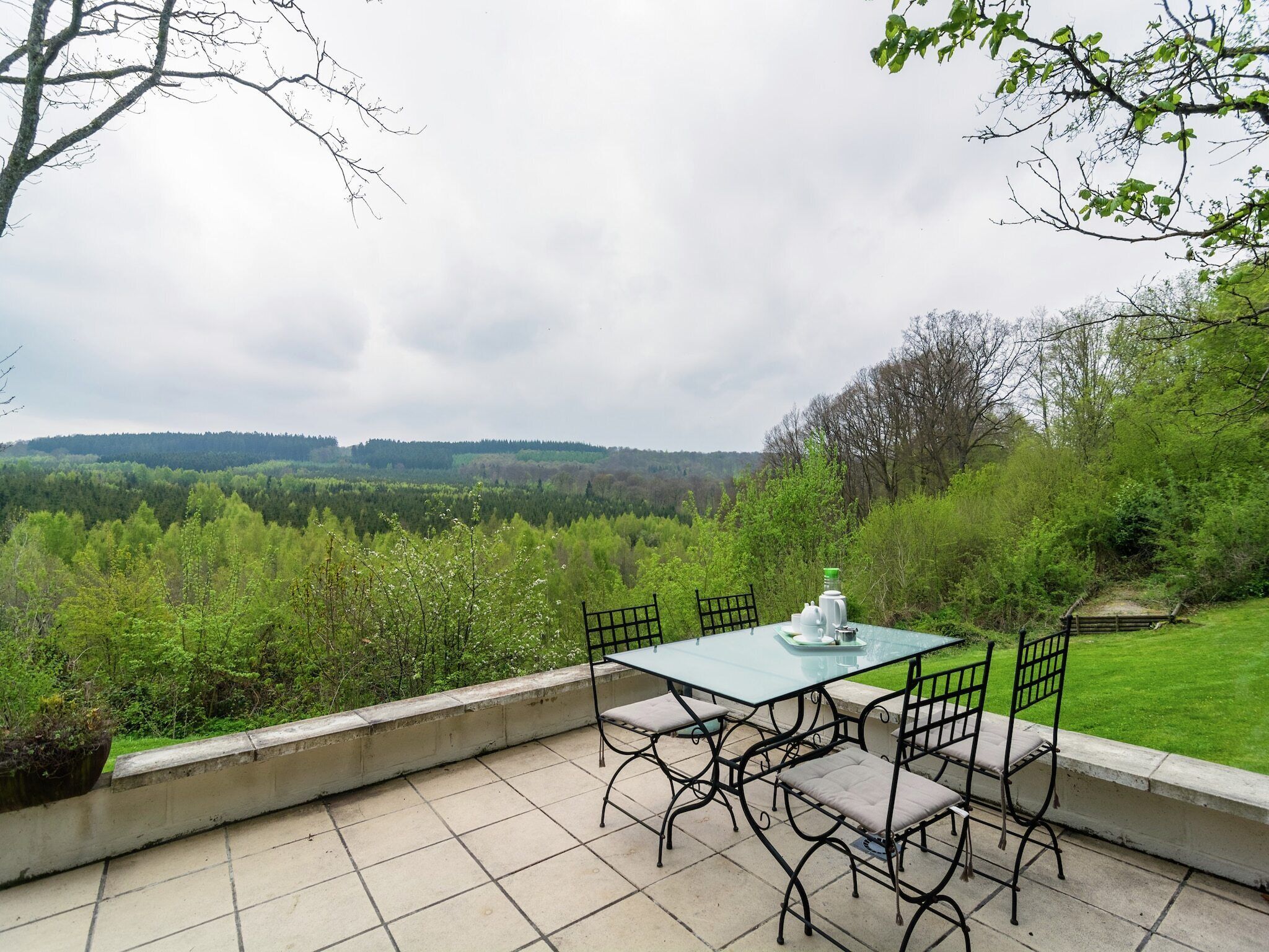 Eine Terrasse im Freien mit Tisch und Stühlen, umgeben von einer Aussicht auf eine bewaldete Landschaft.