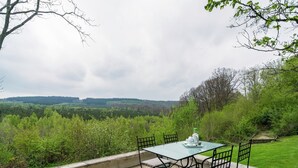 An outdoor patio with a table and chairs, surrounded by a view of a forested landscape. - Cozy Forest Cottage in Awenne (Awenne)