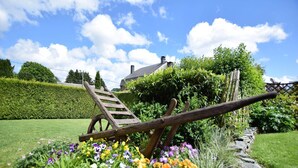 Un jardin avec une brouette en bois, des fleurs et une maison en arrière-plan.