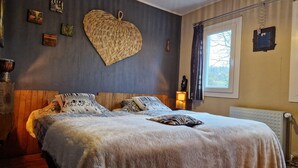 A cozy bedroom with a large bed, a heart-shaped wall decoration, and a window with curtains.
