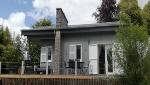 A two-story house with a stone chimney, white shutters, and a fenced patio area.