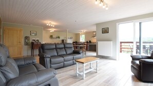 Ein großzügiges Wohnzimmer mit einer Ledersofa, einem Holztisch und einem Essbereich, im Hintergrund ist eine Küche zu sehen.