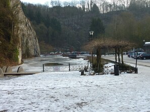 Un espace de stationnement enneigé, avec une rivière, une barrière de sécurité et un banc.
