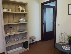 A hallway with a wooden bookshelf, a small round table with a plant, and a door with frosted glass.