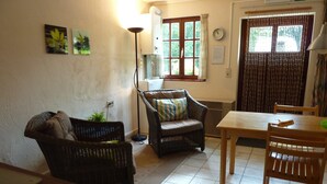 A cozy living room with wicker furniture, a dining table, and a window with curtains. - Cozy Escape in Bohon (Bohon-Durbuy)