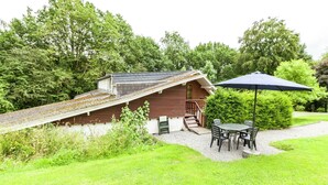A wooden cabin with a sloped roof, a small porch, and a table with chairs under a blue umbrella. - Cozy Escape in Bohon (Bohon-Durbuy)