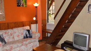 Una sala de estar con una escalera de madera, un sofá floral, una mesa de madera con un cuenco, una lámpara y un televisor.