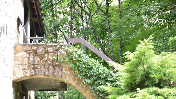 Un puente de piedra con pasarela de madera, rodeado de frondosos árboles verdes.