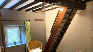 Un dormitorio con techo inclinado, ventana con vistas, una silla de mimbre y una cama con colcha estampada.