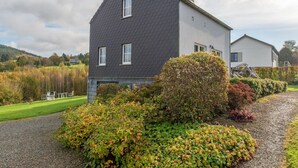Een twee verdiepingen tellend huis met een donker dak en witte muren, omgeven door een verzorgde tuin en een oprit met grind.