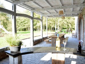 Un patio techado al aire libre con una mesa de madera, una planta en maceta y una botella de vino.